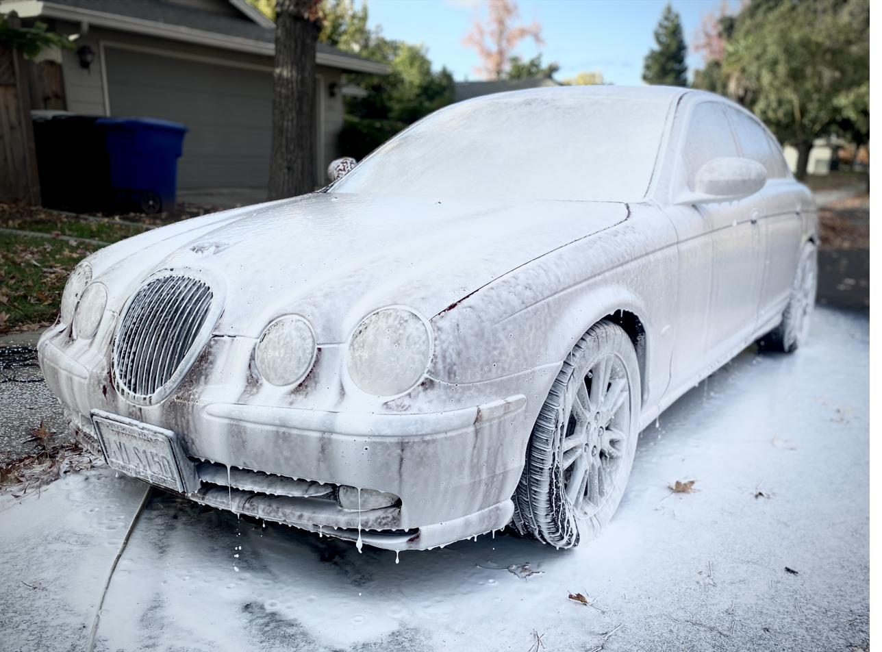 Jaguar sedan covered in thick white snow foam during an exterior detail in a customer's driveway