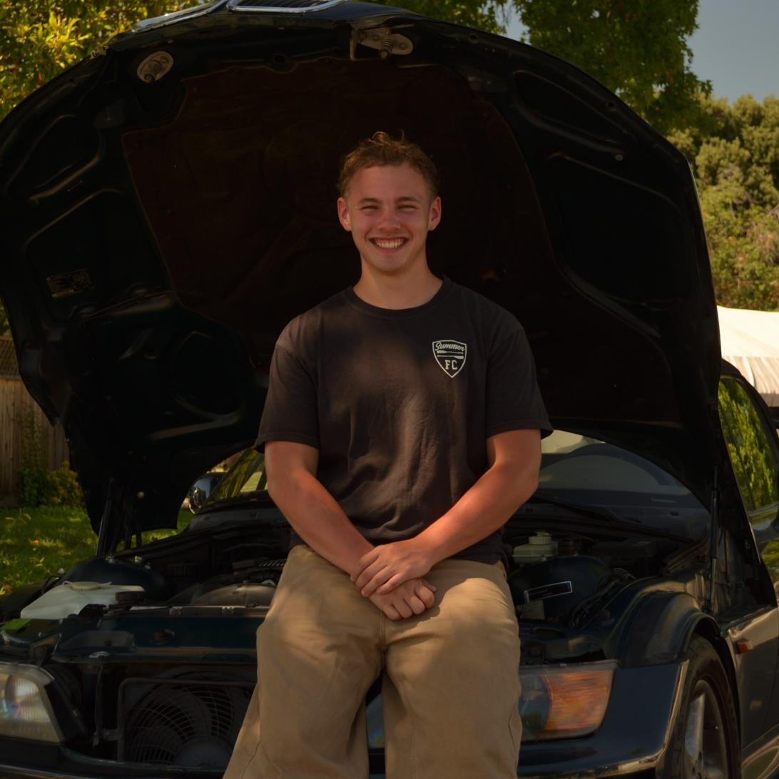 Max Murphey, owner of Murphey Detailing, seated in the engine bay of a BMW Z3